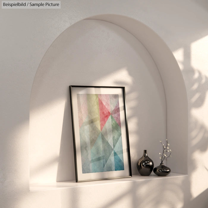 Framed geometric abstract art with pastel colors in arched wall nook, lit by natural sunlight, beside a vase.