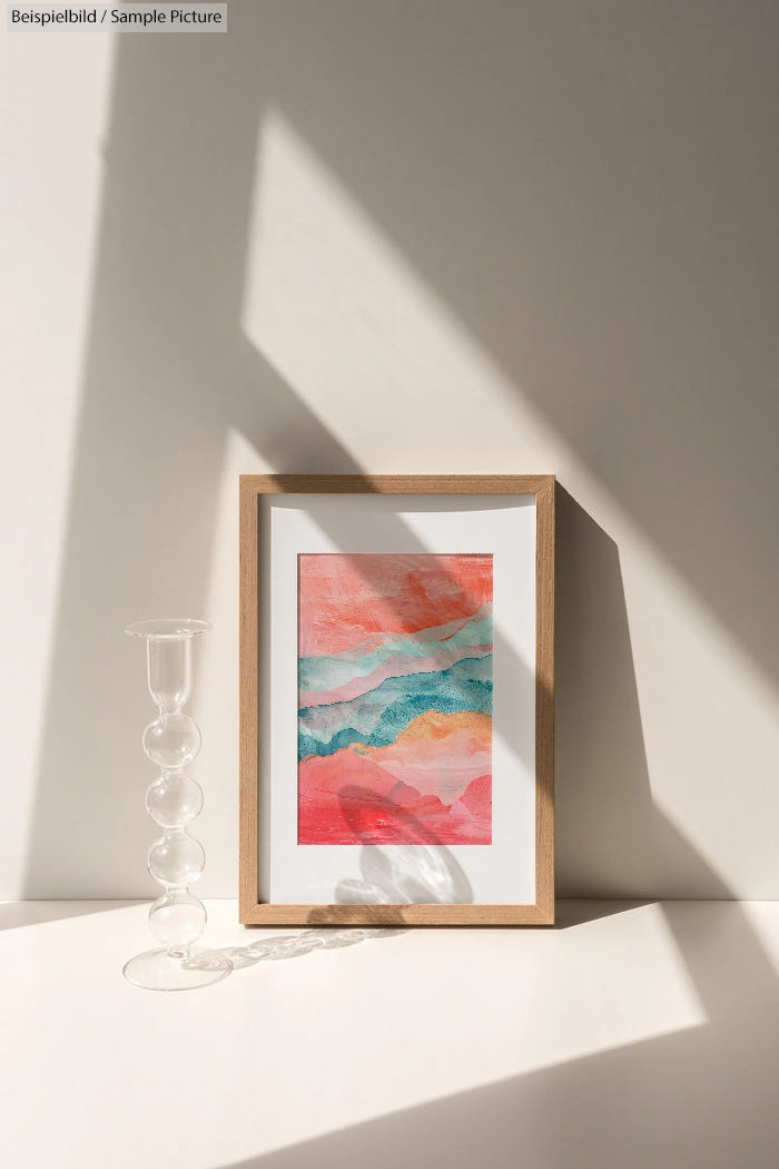 Framed abstract art with pink and teal waves, next to a clear glass candle holder, set against a light background.