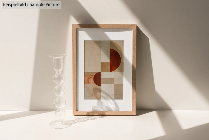 Framed abstract art with geometric shapes beside a bubble-shaped glass vase casting shadows.