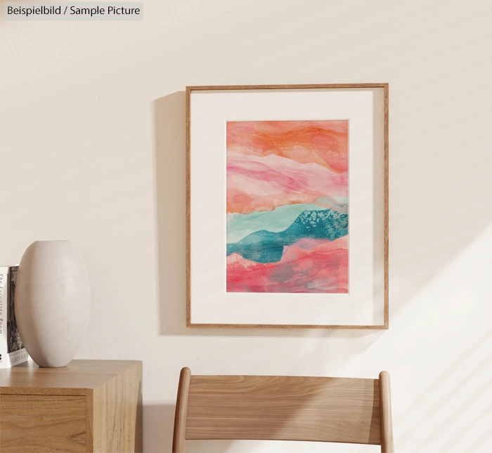 Framed abstract watercolor painting in orange and teal hues, hanging on a light wall beside a minimalist wooden desk and chair.