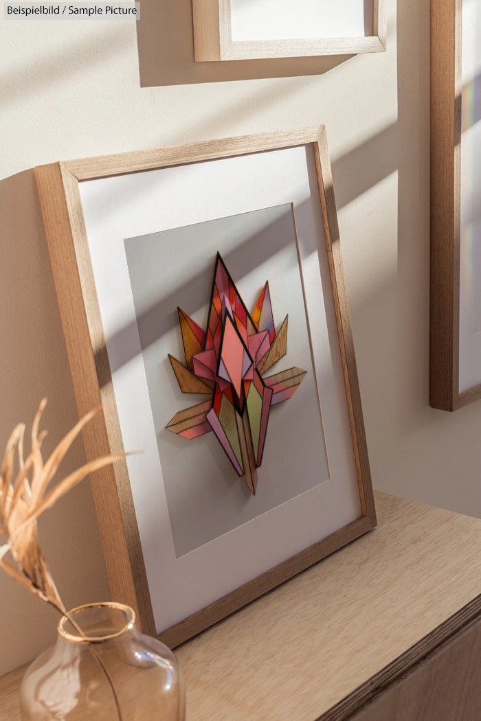 Framed geometric wall art with colorful polygon shapes in a wooden frame on a display shelf.