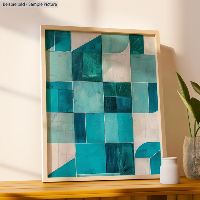 Abstract geometric painting in shades of teal and white in a wooden frame on a wooden shelf with a potted plant.