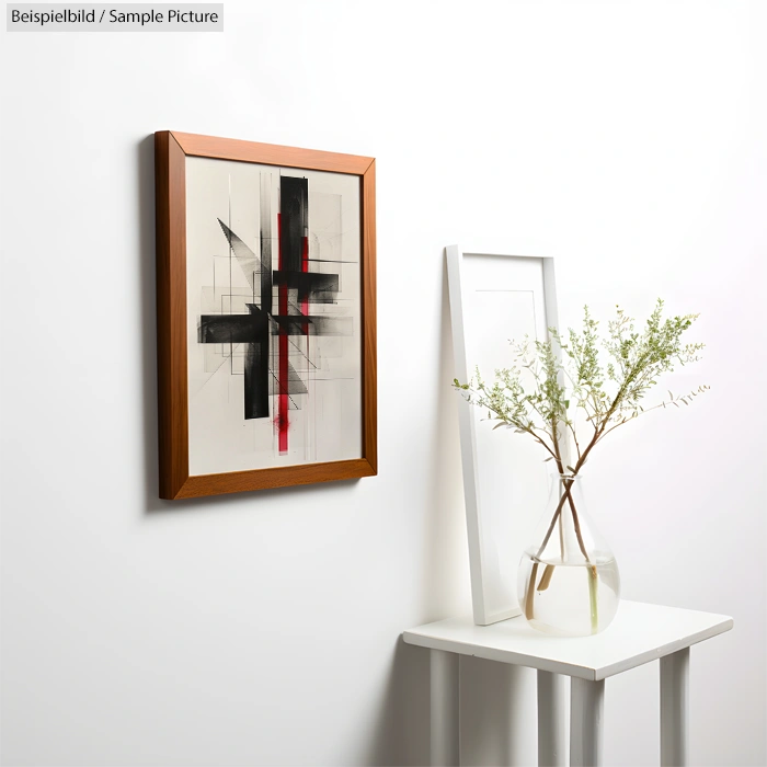 Framed abstract painting on wall with geometric black and red shapes, next to a vase with branches on a small table.