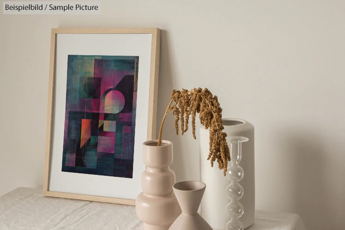 Modern abstract artwork with geometric shapes next to vases with dried flowers on a minimalist white surface.