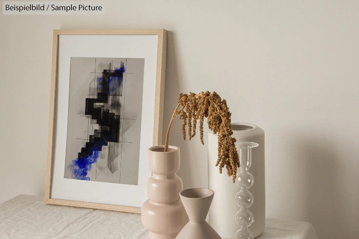 Modern abstract framed art with blue and black accents beside sculptural vases on a neutral background.