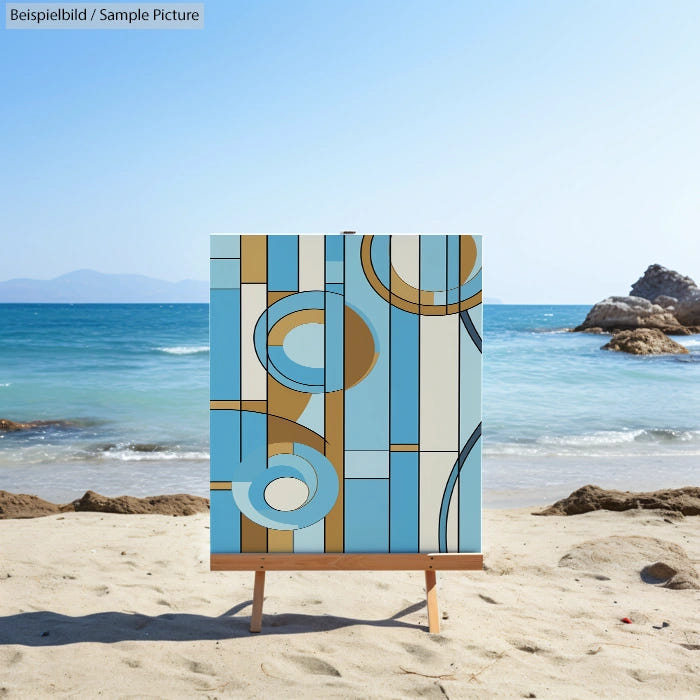 Abstract painting with blue and tan geometric shapes on easel by the beach.