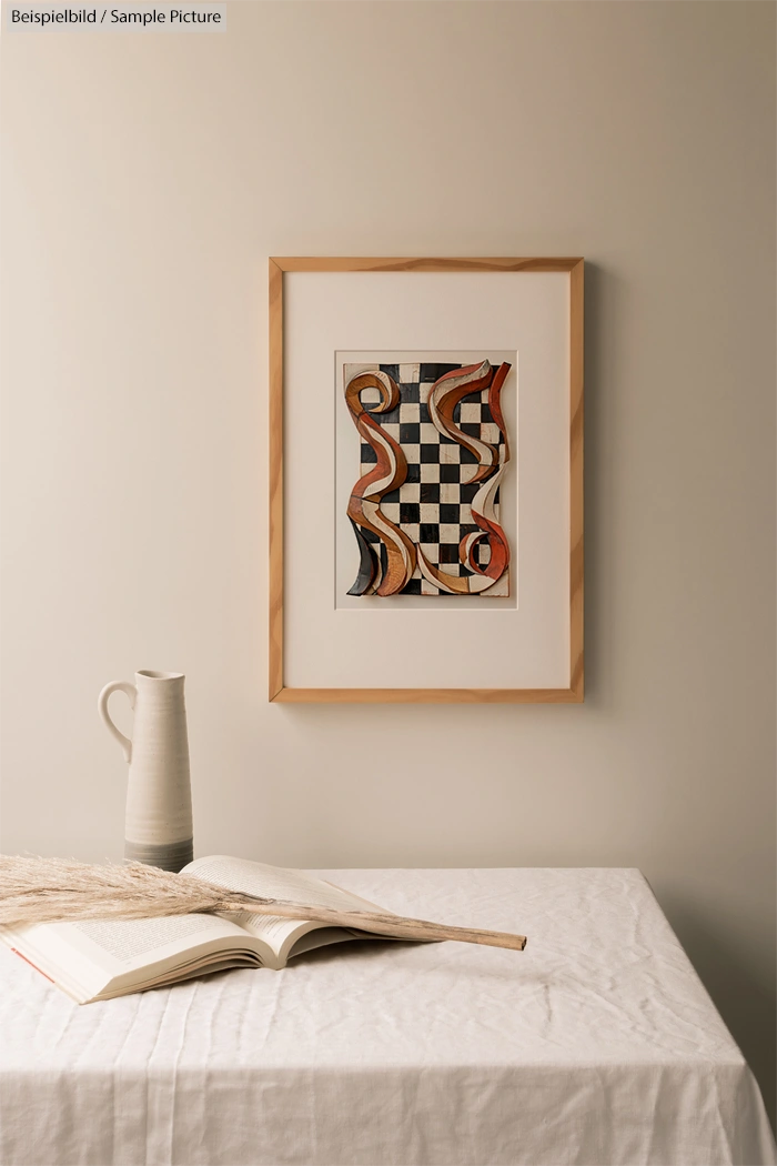 Framed abstract art with red and orange swirls on checkered background, next to an open book on a table with a vase.