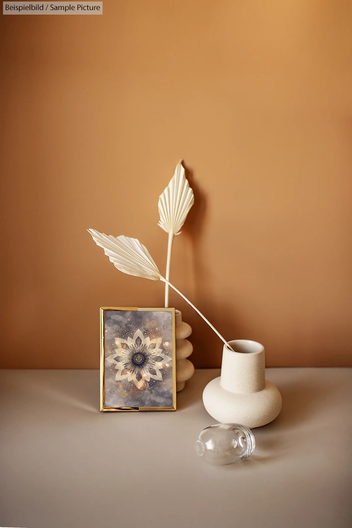 Minimalist still life with dried leaves, small painting, and white ceramic vases against a warm brown background.