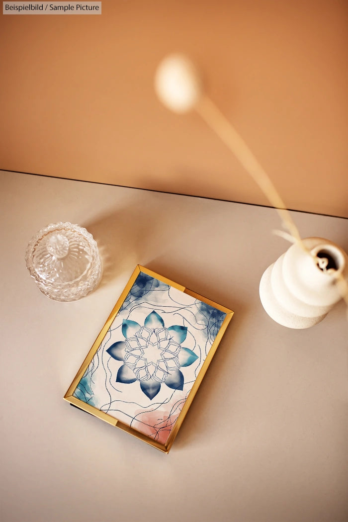 Decorative sketch of a blue lotus with abstract lines, placed in a wooden frame on a beige table near a crystal glass.