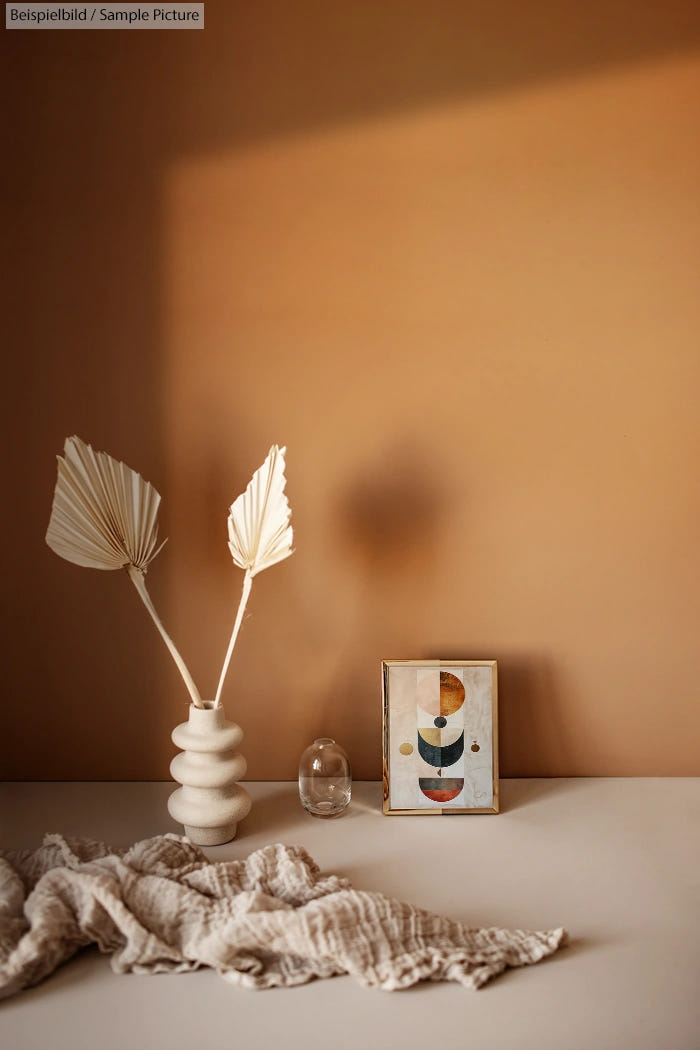 Minimalist interior decor with palm frond vase, abstract art, and textured cloth on a beige background.