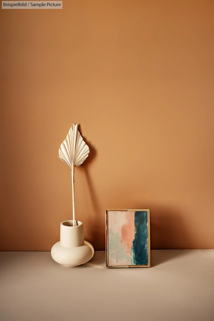 Minimalist decor with a beige vase and abstract painting on a beige surface against a taupe wall.