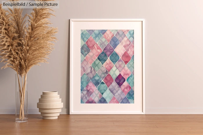 Framed geometric art with pastel colors next to dried pampas grass and a white ceramic vase on wooden floor.