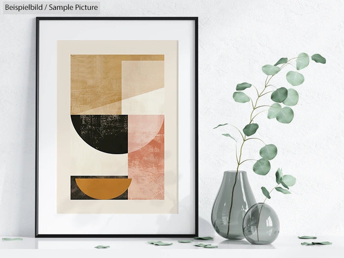 Framed abstract geometric print with beige, black, and pink shapes, beside modern vase with eucalyptus branches.