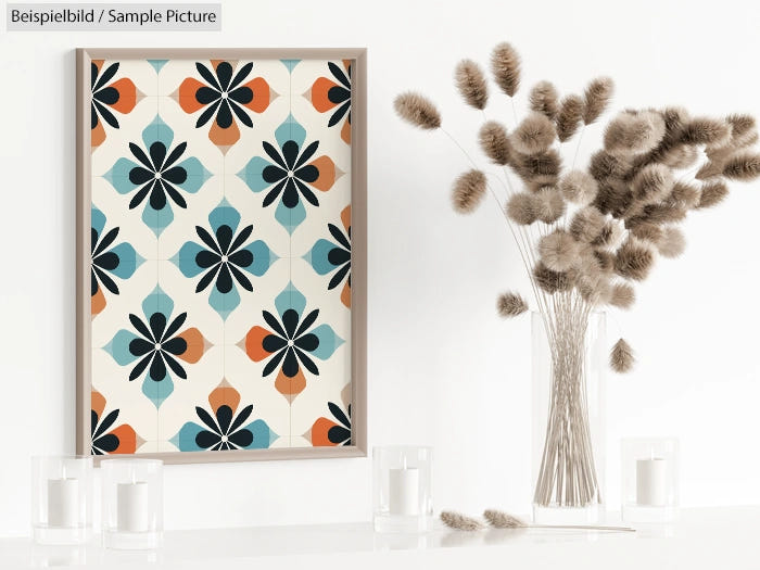 Decorative wall art with geometric floral pattern beside a vase of dried grasses on a white surface.