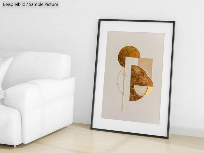 Abstract framed artwork with gold geometric shapes leaning against a white wall near a white sofa.