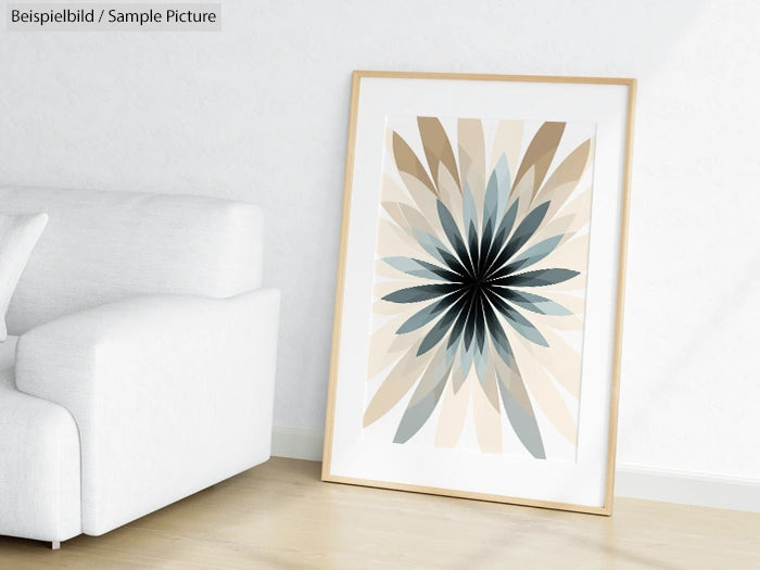 Framed abstract art with radial pattern in beige and blue hues, leaning against a white wall near a sofa.