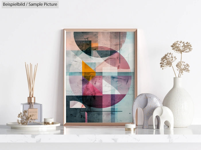 Modern geometric art print in wooden frame on a white shelf with decorative vases and reed diffuser.