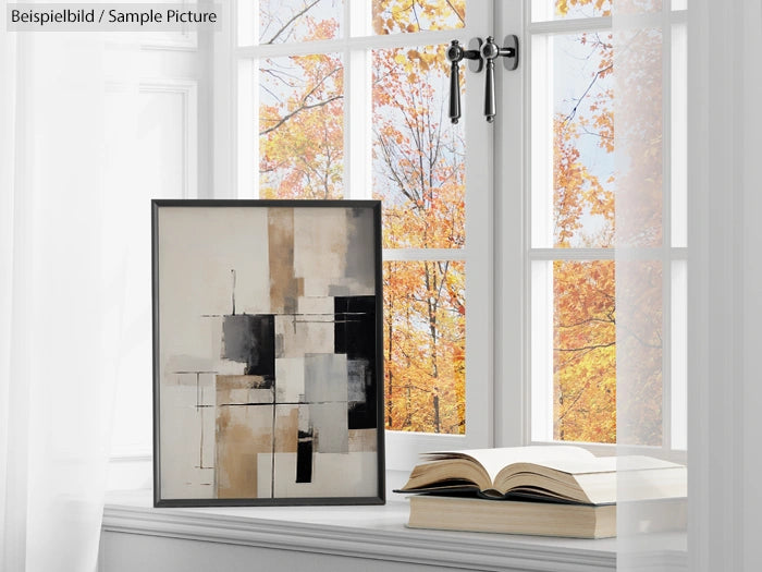 Framed abstract painting on windowsill with open book; autumn trees visible through window.