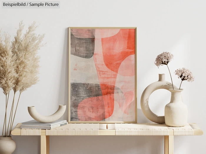 Minimalist abstract art in pink and gray, framed on a wooden table with dried flowers and white ceramic vases.