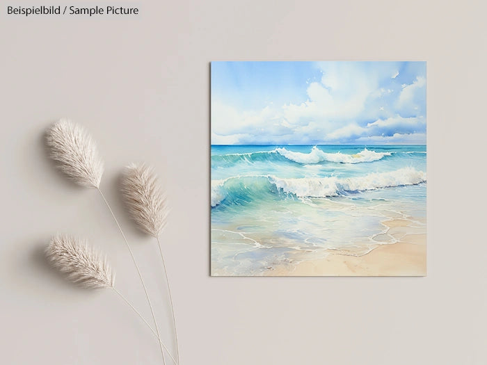 Wall art of a beach scene with waves, clouds, and sky, placed on a beige wall next to fluffy dried flowers.