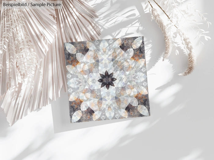 Geometric art print with symmetrical floral pattern in muted earth tones, displayed on a white surface with dried leaves.