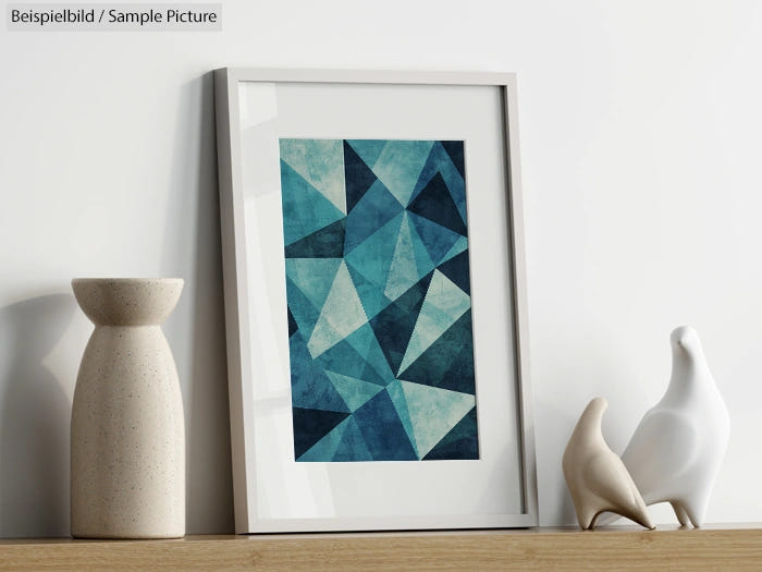 Geometric abstract art in blue tones, framed and placed on a wooden shelf beside white ceramic vases and bird figures.