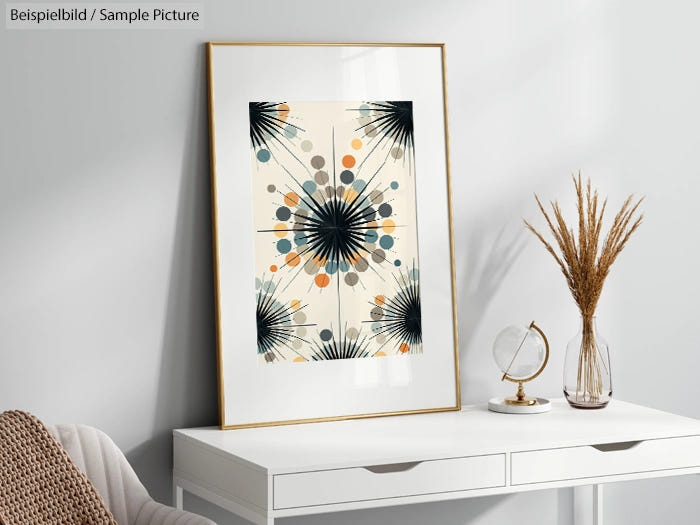 Modern abstract art print with geometric and floral motifs on a white desk with globe and dried plant decorations.