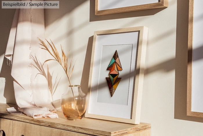 Framed abstract art with geometric design on a wooden cabinet, lit by natural window light with shadows.