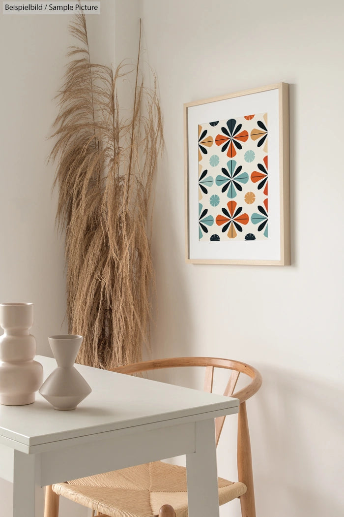 Minimalist dining area with dried reed decor and framed geometric art on wall, featuring chairs and a small white table.