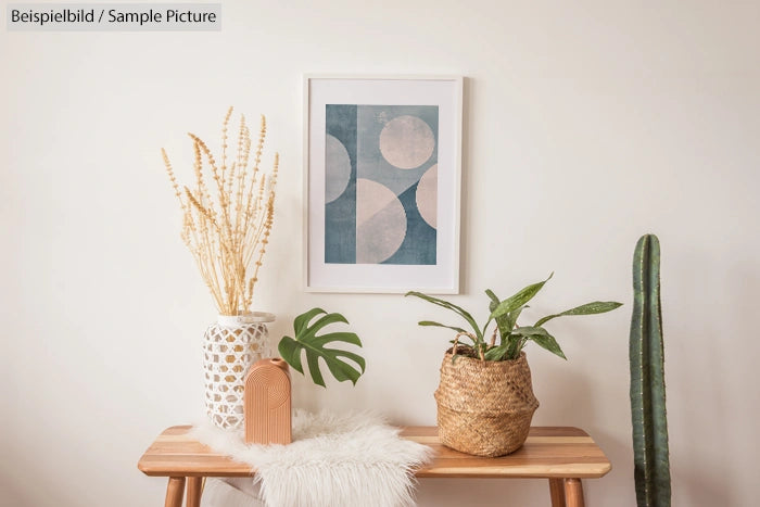 Minimalist decor with framed abstract art, plants, wooden table, and textured vase against a plain wall.