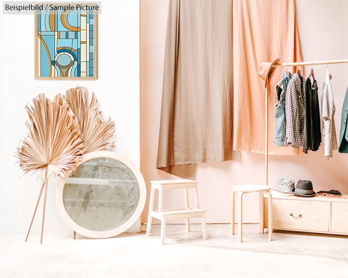 Minimalist interior with clothing rack, dried palm leaves, round mirror, and abstract art on wall.