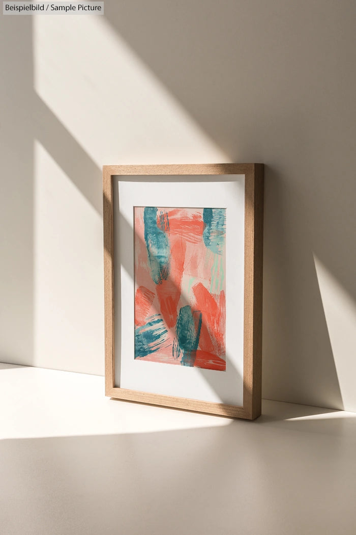 Framed abstract painting with green and blue brushstrokes on a pink background, set on a sunlit table.