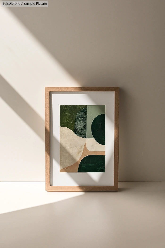 Framed abstract art print on a sunlit wall featuring green, beige, and dark shapes.