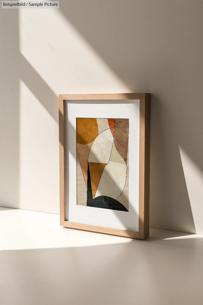 Framed abstract art with geometric shapes in warm tones, placed on a white surface with sunlight and shadows.