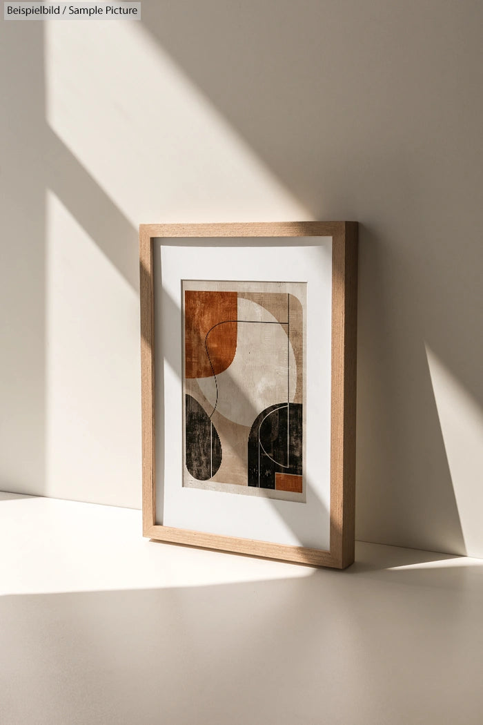 Framed abstract art with geometric shapes in neutral tones, placed on lit surface with shadow play.