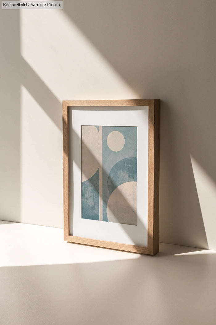 Wooden framed abstract art with blue and beige geometric shapes, lit by sunlight casting shadows.