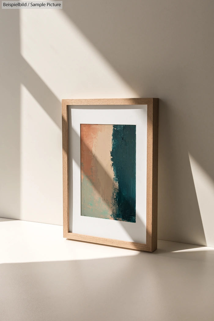 Framed abstract painting with beige and dark teal vertical sections, placed on a sunlit white shelf.