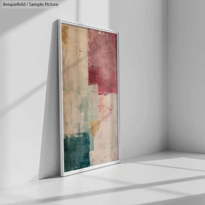 Framed abstract painting with red, pink, and teal blocks, leaning against a white wall in a well-lit corner.