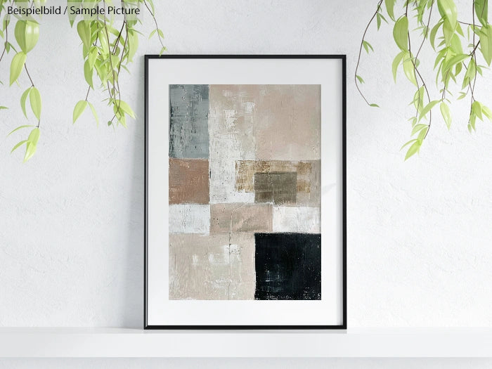 Framed abstract artwork with beige, gray, and black geometric shapes, hanging on a white wall with greenery above.