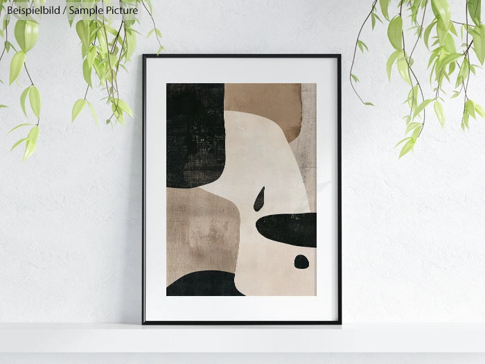 Framed abstract art with geometric shapes in beige, black, and brown tones, hanging on a white wall with green plants.