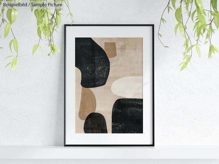 Framed abstract art with overlapping beige and black shapes, displayed on a white wall with hanging green plants.