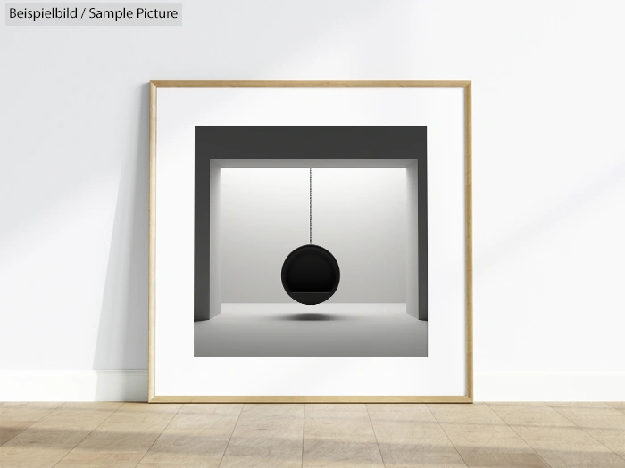 Framed minimalist art of a black sphere hanging in a white room, displayed against a white wall.