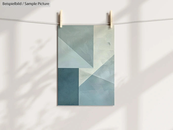 Geometric abstract painting in shades of blue and gray hanging on a line with clothespins.