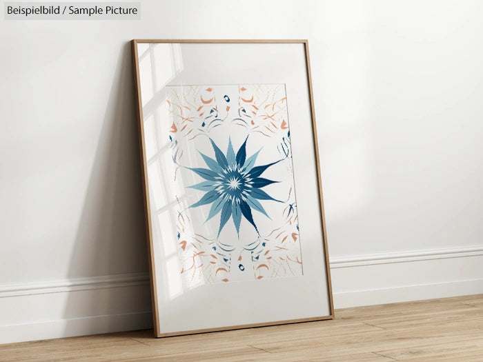 Framed art print with geometric blue and orange star design, leaning against a white wall on a wooden floor.