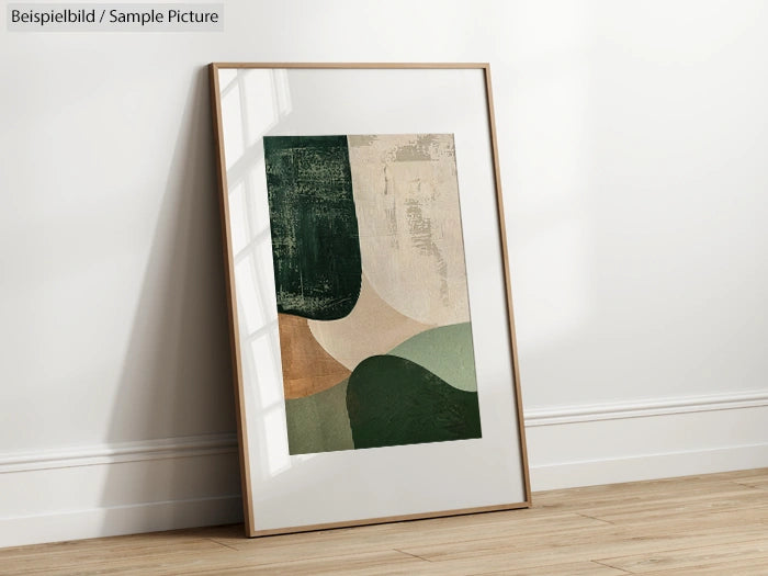 Framed abstract art print on floor, featuring green, beige, and brown geometric shapes, leaning against a white wall.