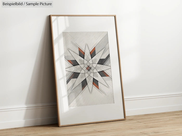 Framed geometric star artwork with gray, black, and orange accents leaning against a white wall on wooden floor.