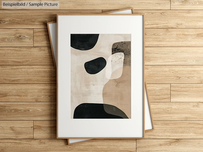 Abstract art print with black, white, and beige shapes in wooden frame on wooden floor.