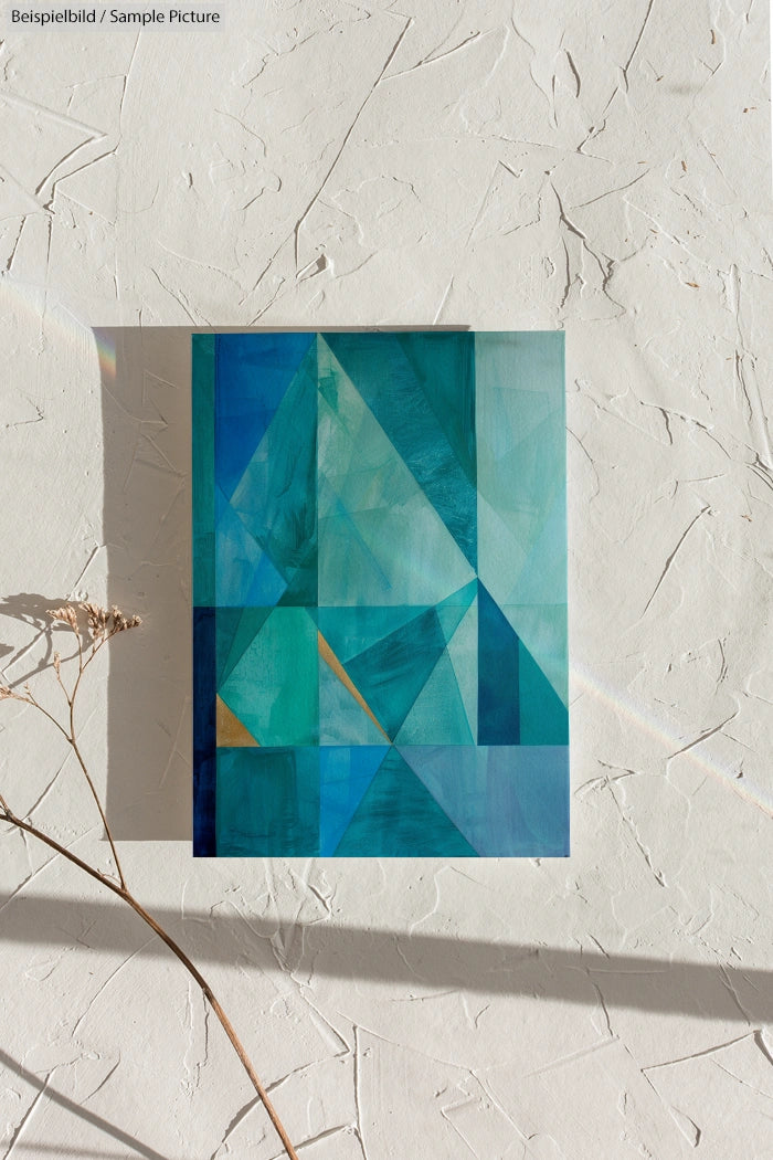 Geometric abstract artwork with blue and green triangles on a textured white wall; shadow of plant on the wall.