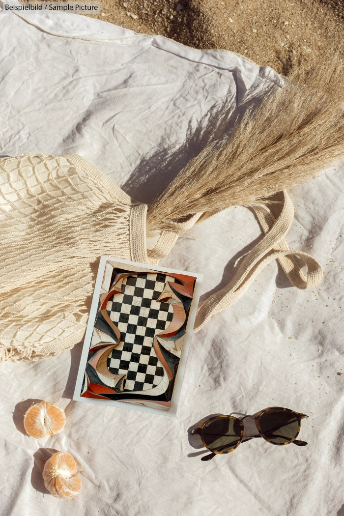 Beach scene with bag, decorative box, sunglasses, and peeled oranges on a white cloth and sand.