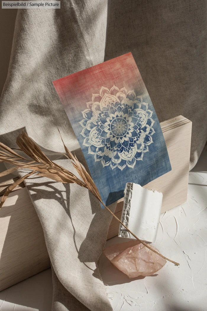 A mandala design on a red-blue gradient card placed on fabric with pampas grass and crystal decor.